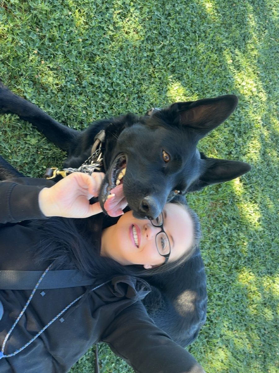 Velma, owner of Howl 4 Us, lying in the grass with her German Shepherd